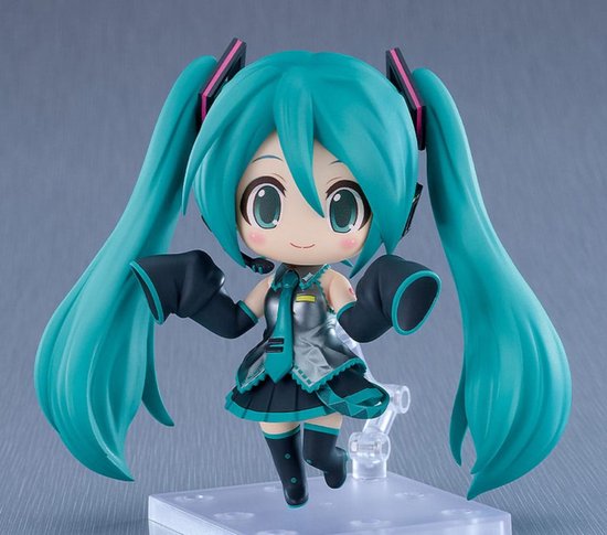 A chibi-style Hatsune Miku figurine with long turquoise twin tails, a black and teal outfit, and pink ear tips, posed on a clear display stand against a soft gray background.