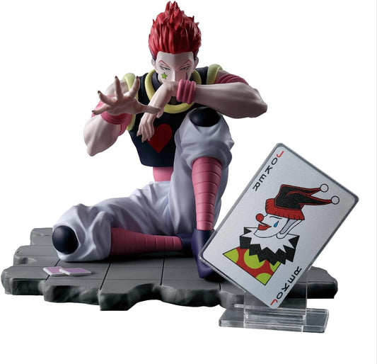 A collectible figurine of the character Zenitsu Agatsuma from Hunter x Hunter, posed sitting on a dark gray stone-like base with a tilted playing card displaying his face. The figure has spiky red hair, pale skin, and wears a black vest with a red heart, white pants, and pink striped socks, set against a plain white background.