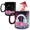 A black ceramic mug shown in two views on a white background: one view shows the mug with a black handle and a dark printed design, and the other shows the mug transformed with a colorful gradient design featuring a large white headphone graphic, pink and white Japanese text, and the name 'MATSUNE MIKU'. A red arrow with °C/F text indicates a temperature-change effect.