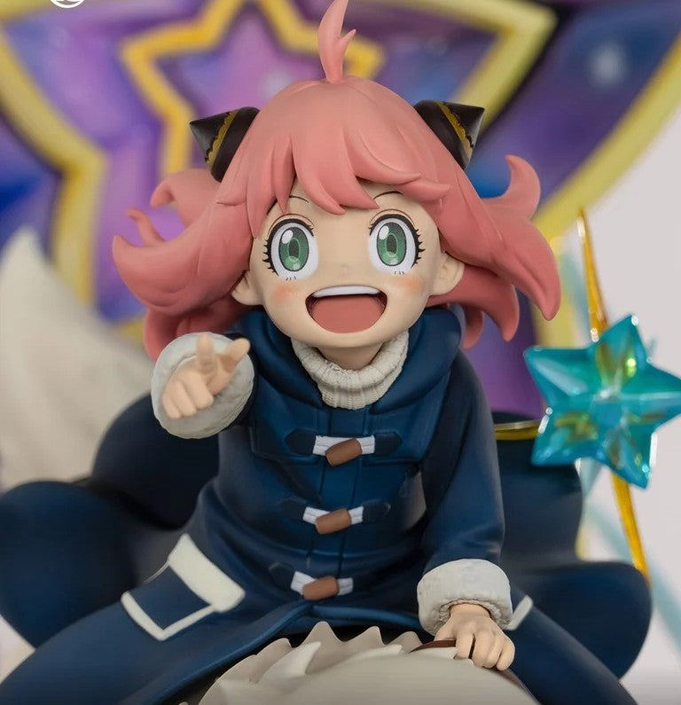 A collectible anime figurine of Anya Forger from My Hero Academia, wearing her signature blue winter coat and pink hair, posed sitting down with a star-shaped accessory.