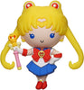 Toy figure of a character with blonde hair, blue eyes, and a red and white outfit holding a pink and yellow weapon on a white background.