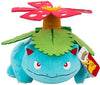 A blue plush toy resembling Bulbasaur from Pokémon, with a green leaf on its back and a red flower growing from it. A Pokémon tag is attached on the right side, set against a plain white background.
