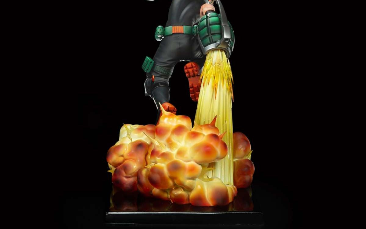 A detailed collectible statue of a sci-fi character in black and green armor, launching a powerful stream of yellow energy or flame from their hands, creating a large orange and yellow explosion on a black base against a solid black background.