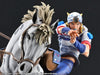 A detailed collectible figurine of a blonde character in a blue and white outfit riding a white horse, posed against a dark background. The figure is pointing forward with one hand while holding the reins with the other.